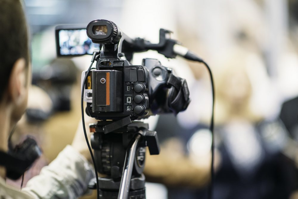 Public Relations Television camera recording publicity event. Camera in focus, operator and event blurred
